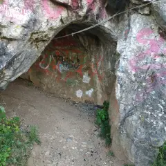 Wejście do jaskini w rezerwacie przyrody Kadzielnia, pokryte graffiti. Stalowa lina biegnie nad wejściem.