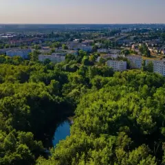 Zielone tereny rezerwatu przyrody Żurawiniec otaczają osiedle mieszkaniowe. Widać rzekę i drzewa.
