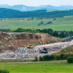 Góra śmieci na wysypisku, gdzie pracownik zastanawia się, ile kosztuje tona śmieci na wysypisku. W tle zielone wzgórza.