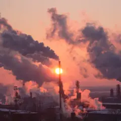 Zachodzące słońce przebija się przez gęste kłęby dymu z kominów fabrycznych, tworząc widok, który pokazuje, co to jest smog.