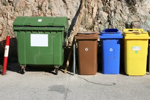 Kolorowe kontenery na śmieci stoją pod skalistą ścianą. Zastanawiasz się, dlaczego wywóz śmieci drożeje?