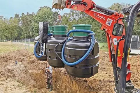 Koparka Kubota montuje zbiorniki oczyszczalni biologicznej. Czasem pojawia się pytanie, dlaczego śmierdzi z oczyszczalni biologicznej, ale tu widzimy proces instalacji.