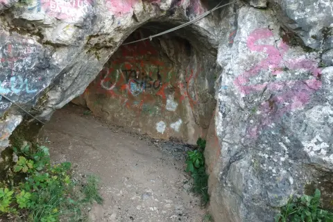 Wejście do jaskini w rezerwacie przyrody Kadzielnia, pokryte graffiti. Stalowa lina biegnie nad wejściem.