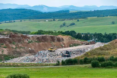 Góra śmieci na wysypisku, gdzie pracownik zastanawia się, ile kosztuje tona śmieci na wysypisku. W tle zielone wzgórza.