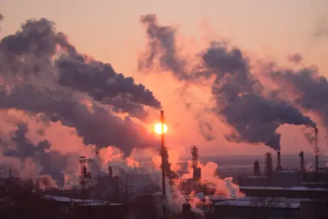 Zachodzące słońce przebija się przez gęste kłęby dymu z kominów fabrycznych, tworząc widok, który pokazuje, co to jest smog.