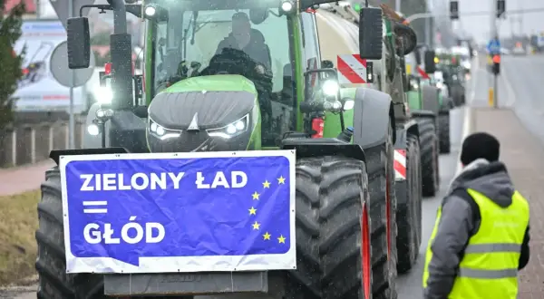 Traktor z banerem "Zielony Ład = Głód" i flagą UE, w tle protestujący rolnicy.