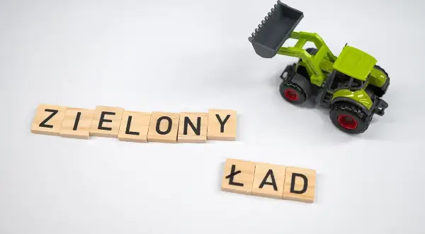 Drewniane klocki z literami "ZIELONY ŁAD" i zielona zabawka koparko-ładowarka na białym tle.