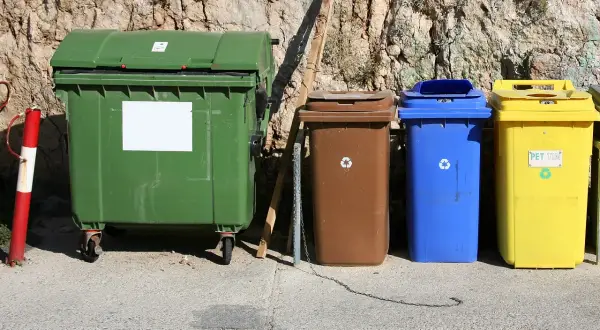 Kolorowe kontenery na śmieci stoją pod skalistą ścianą. Zastanawiasz się, dlaczego wywóz śmieci drożeje?