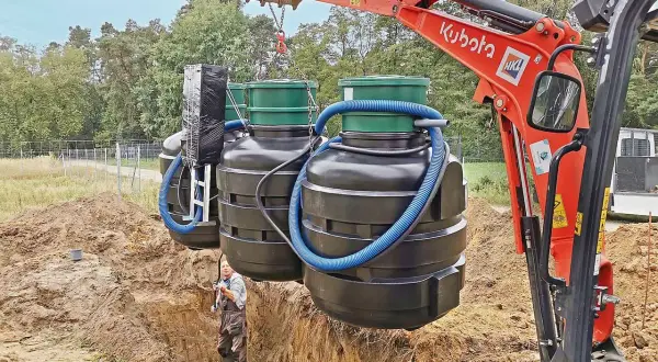 Koparka Kubota montuje zbiorniki oczyszczalni biologicznej. Czasem pojawia się pytanie, dlaczego śmierdzi z oczyszczalni biologicznej, ale tu widzimy proces instalacji.