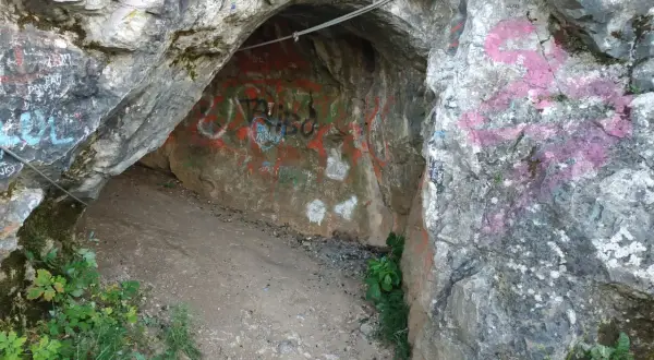 Wejście do jaskini w rezerwacie przyrody Kadzielnia, pokryte graffiti. Stalowa lina biegnie nad wejściem.