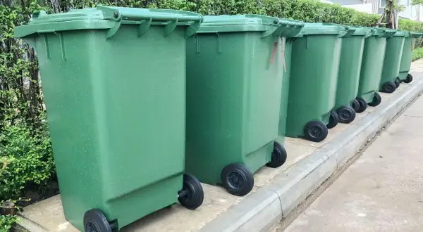 Zielone kosze na śmieci stoją w rzędzie. Segregacja odpadów to klucz do tego, jak uniknąć opłaty za śmieci.