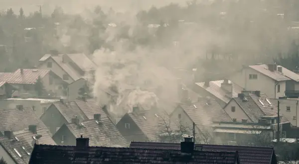 Dym wydobywający się z kominów domów na tle mglistego krajobrazu.