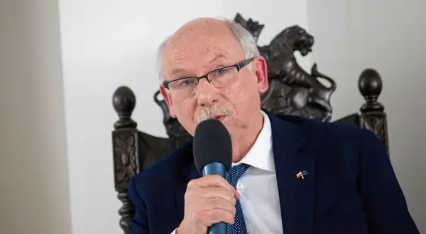 Starszy mężczyzna w okularach i garniturze przemawia do mikrofonu. Na klapie marynarki ma przypinkę z flagami Polski i UE, symbolizującą jego poparcie dla tych, kto głosował za zielonym ładem.