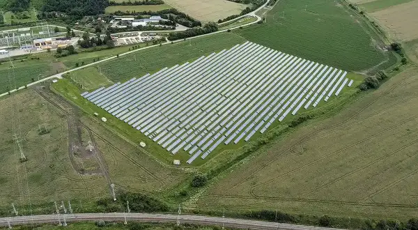 Widok z lotu ptaka na dużą farmę paneli słonecznych otoczoną polami i lasem.