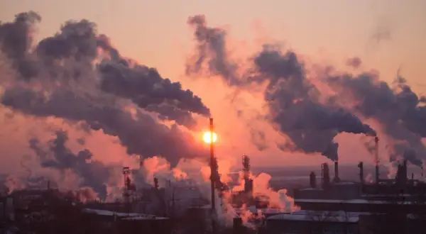 Zachodzące słońce przebija się przez gęste kłęby dymu z kominów fabrycznych, tworząc widok, który pokazuje, co to jest smog.