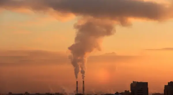 Dym z kominów fabrycznych unosi się na tle zachodzącego słońca, pokazując, przez co powstaje smog.