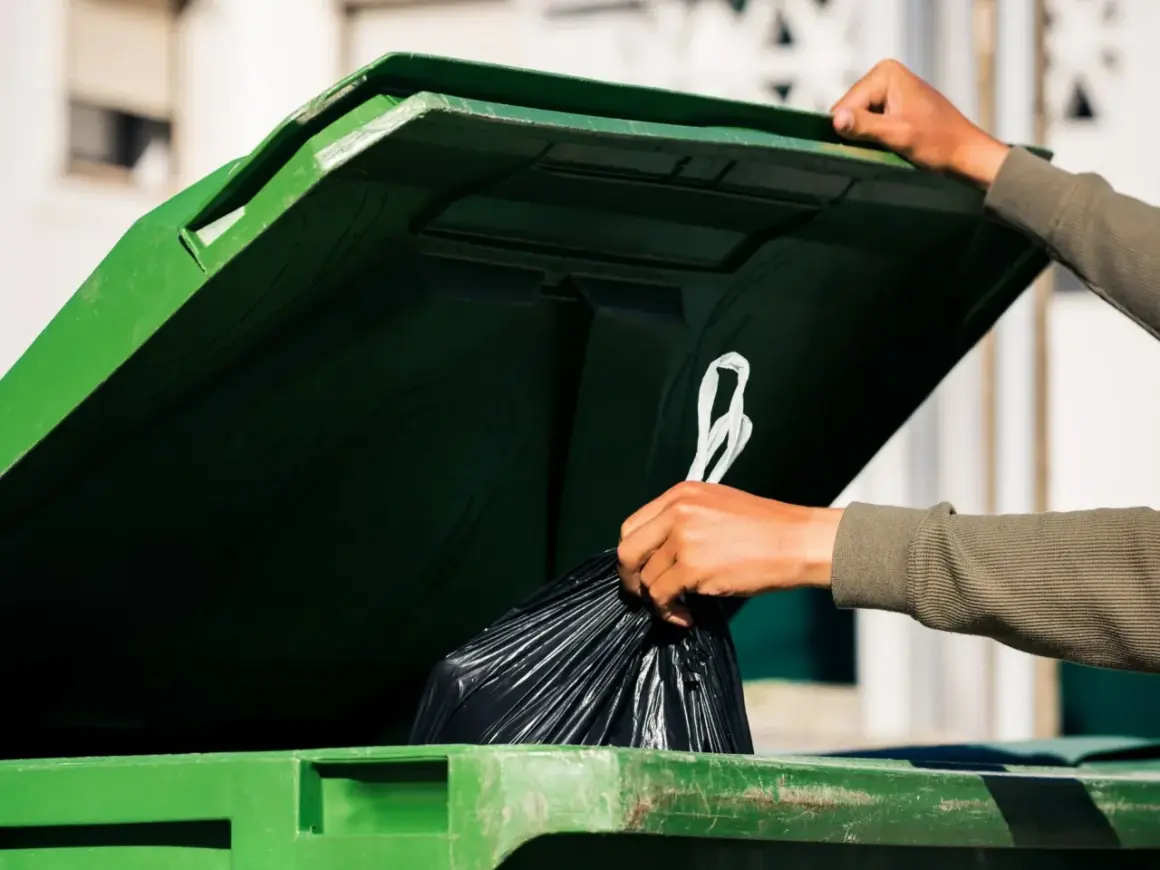 Ręka wrzuca worek ze śmieciami do zielonego kontenera. Kto jest zwolniony z opłaty za śmieci? Może ten, kto segreguje odpady.