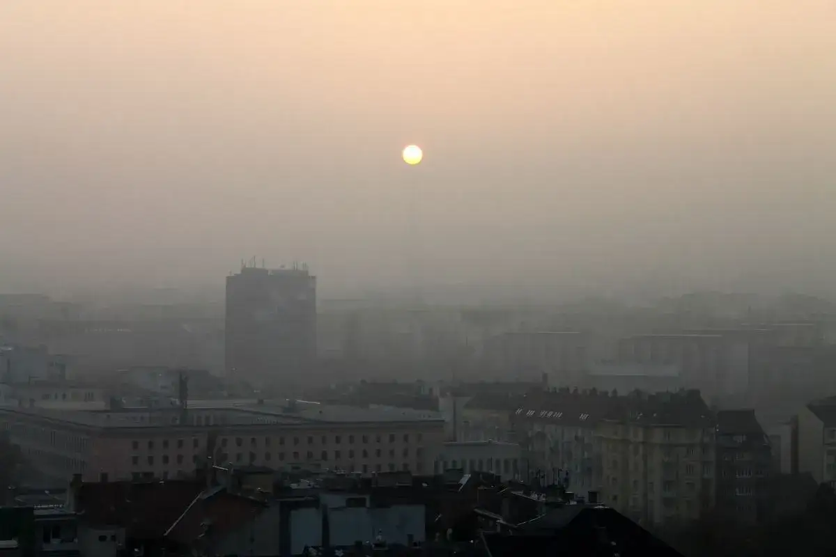 Widok miasta spowitego mgłą, słońce ledwo przebija się przez zanieczyszczenie. Takie widoki przypominają, jakie są rodzaje smogu.