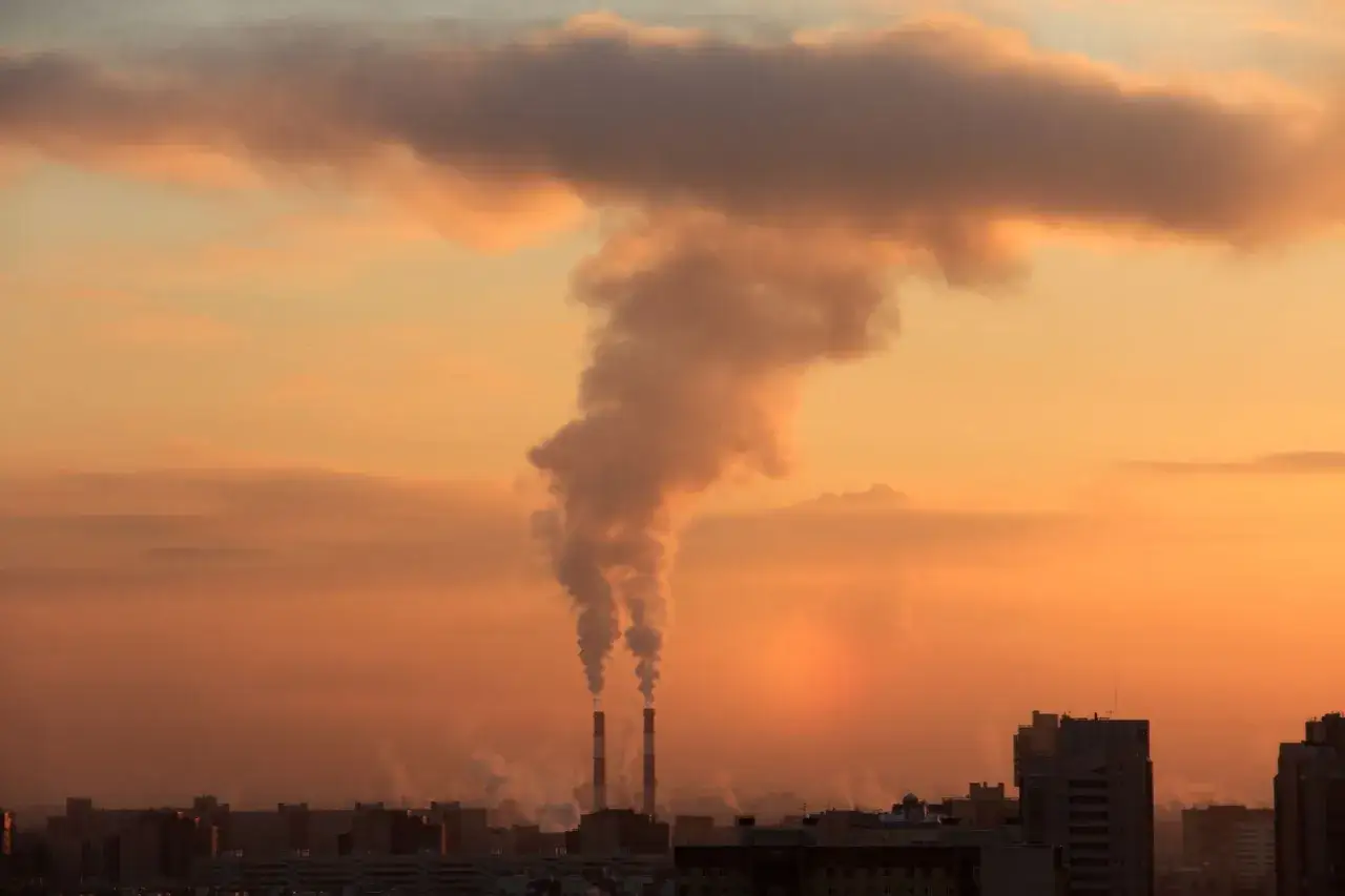 Dwa kominy emitują gęsty dym, tworząc chmurę na tle pomarańczowego nieba. To właśnie co to smog, zanieczyszczenie powietrza.