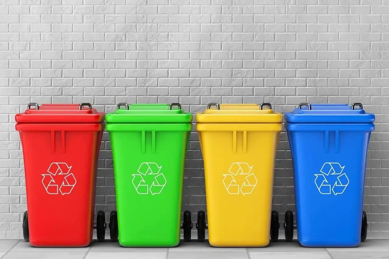 Cztery kolorowe pojemniki na śmieci (czerwony, zielony, żółty, niebieski) z symbolem recyklingu. Ile pojemników na śmieci na osobę?