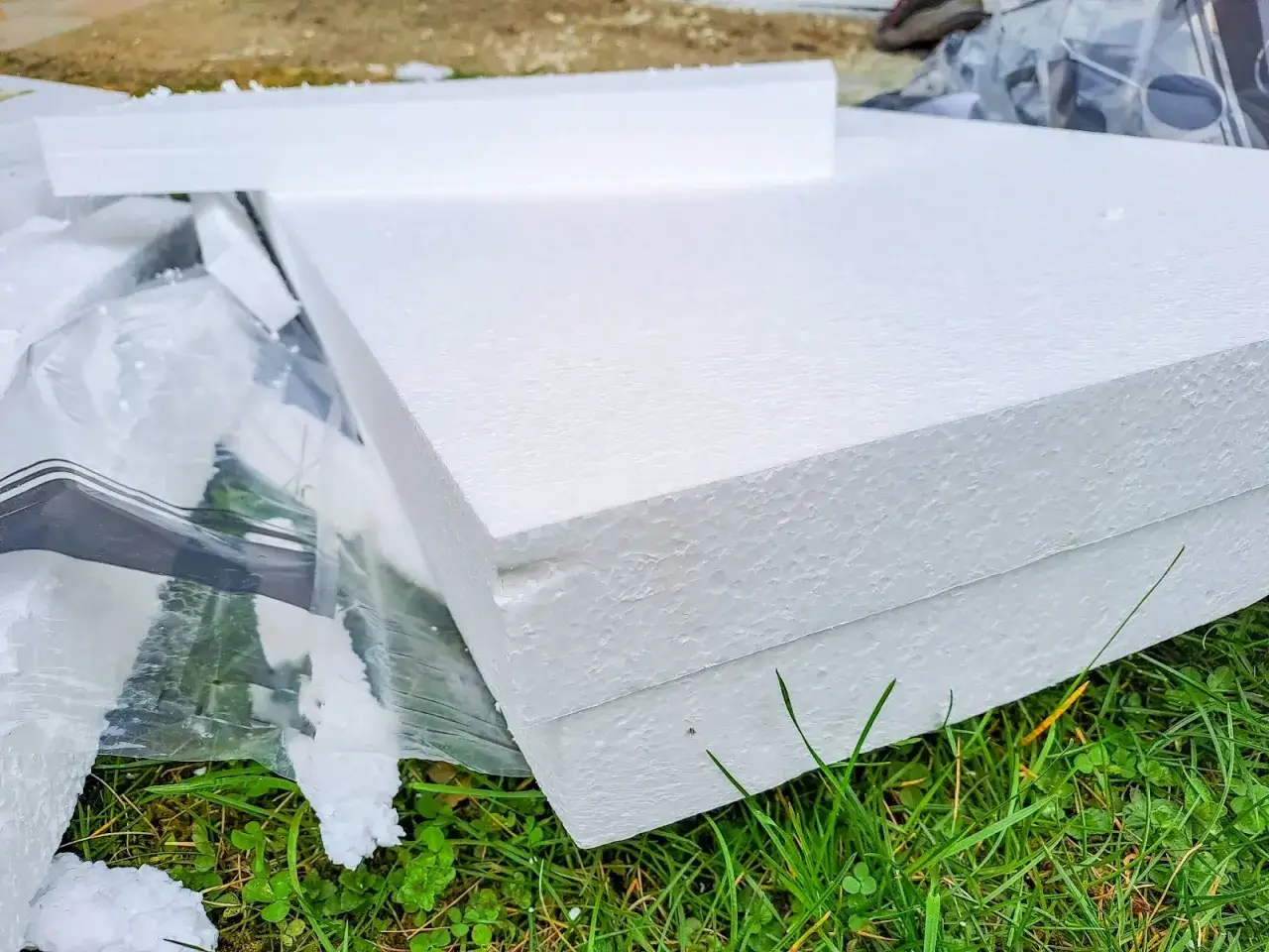 Styropian do jakich śmieci? Białe płyty styropianowe leżą na trawie, częściowo przykryte folią.