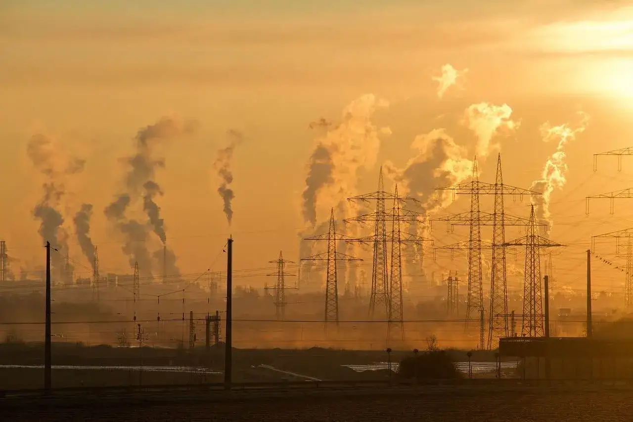 Dymiące kominy fabryk i linie energetyczne na tle zachodzącego słońca. To obraz tego, co to smog, zanieczyszczenie powietrza.