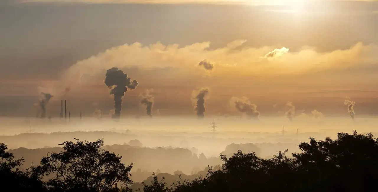 Dymiące kominy fabryk unoszą się nad mglistym krajobrazem, tworząc widok, który pokazuje, co to smog.