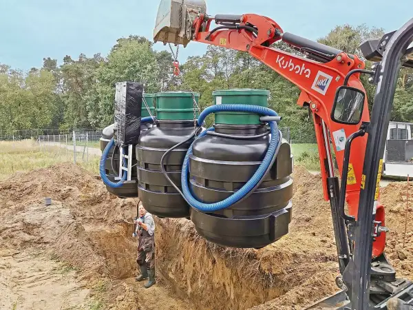 Koparka Kubota montuje zbiorniki oczyszczalni biologicznej. Czasem pojawia się pytanie, dlaczego śmierdzi z oczyszczalni biologicznej, ale tu widzimy proces instalacji.
