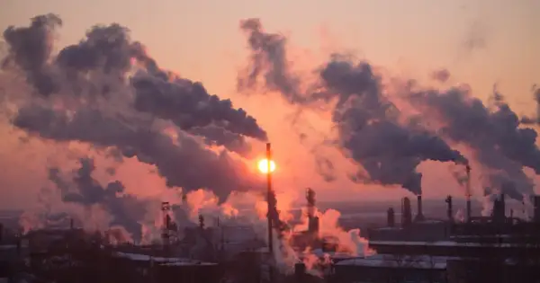 Zachodzące słońce przebija się przez gęste kłęby dymu z kominów fabrycznych, tworząc widok, który pokazuje, co to jest smog.